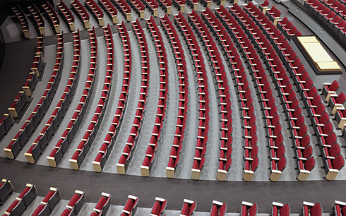 An aerial view of a large auditorium featuring rows of red upholstered seats arranged in a curved pattern.