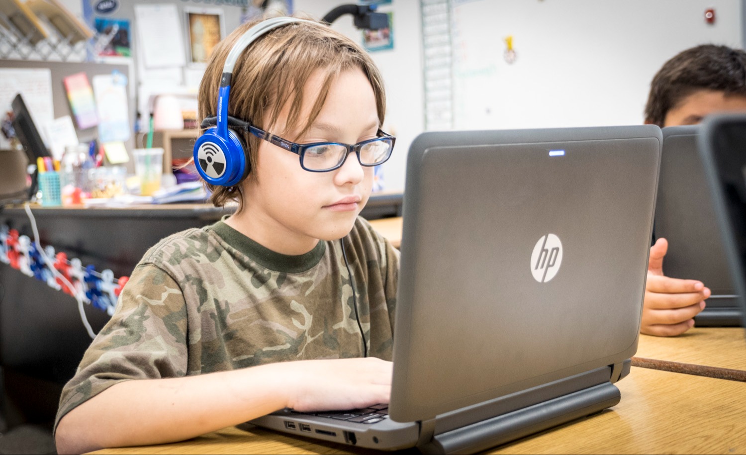 Student sitting at a desk wearing headphones while working on a laptop.