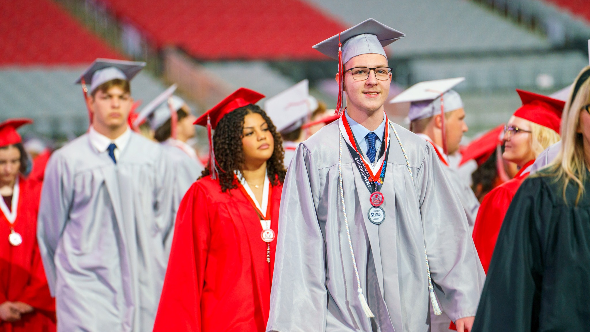 Students in silver and red cap and gowns walking at a graduation ceremony.
