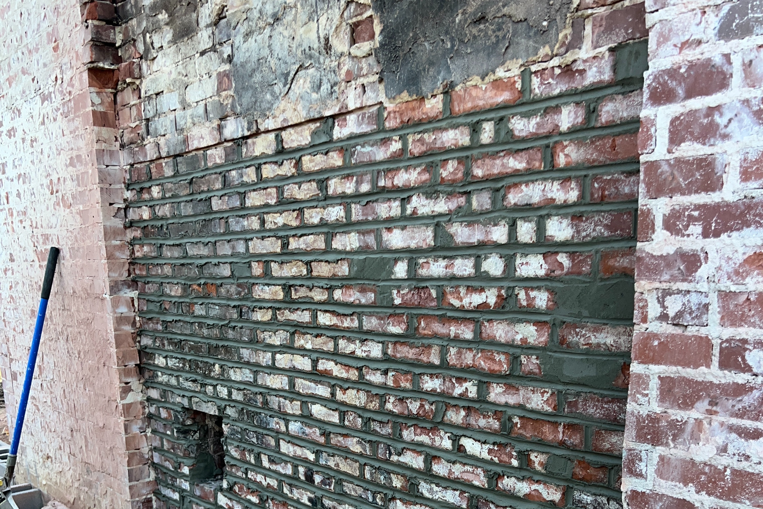 Bare brick wall with additional mortar being placed between older bricks.