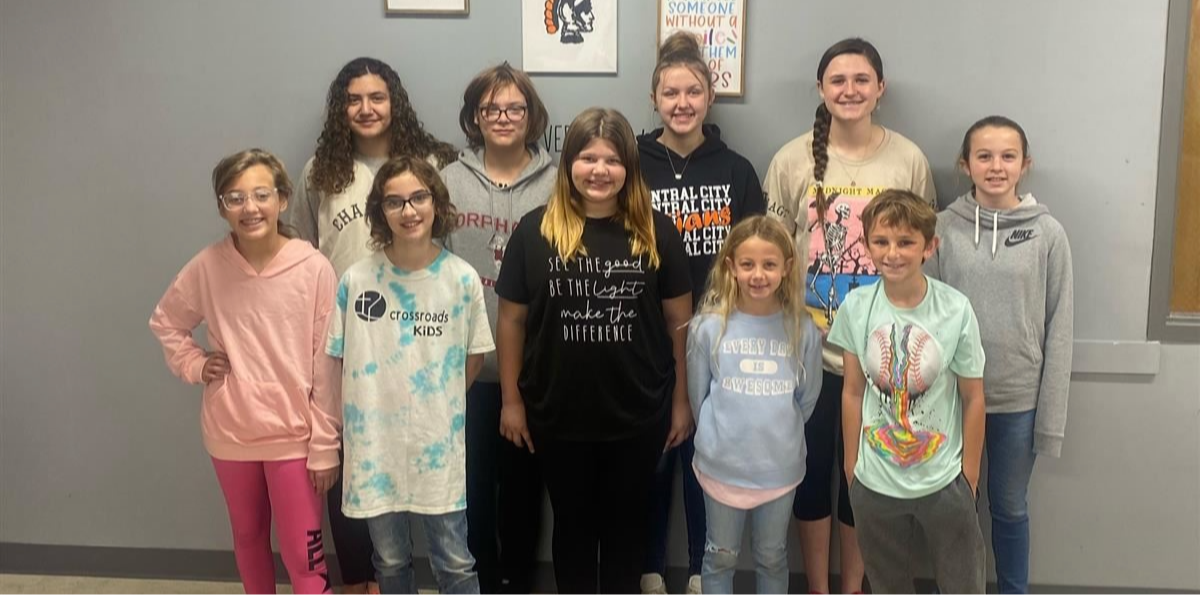 A group of twelve children and teenagers stands together in a hallway, smiling