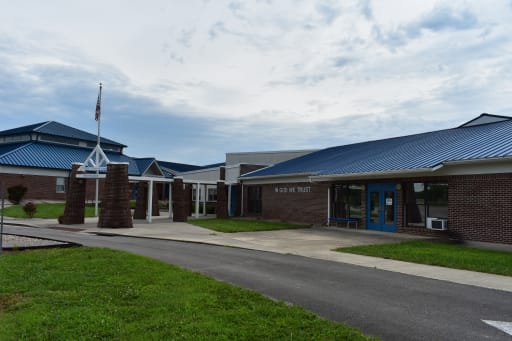 1. Front entrance of a school building featuring a distinctive blue roof, welcoming students and visitors alike. 2. The entrance of a school building, showcasing a vibrant blue roof, inviting students and community members. 3. School building entrance with a prominent blue roof, serving as a welcoming point for students and visitors.