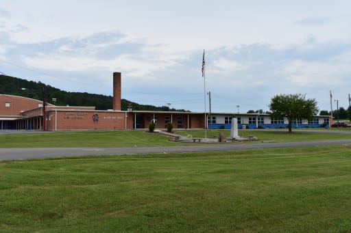 1. A school building stands prominently on a lush grassy field, surrounded by greenery and open space. 2. The school building is situated on a vibrant grassy field, creating a serene educational environment. 3. A school building is positioned on a green grassy field, emphasizing a peaceful and inviting atmosphere for learning.