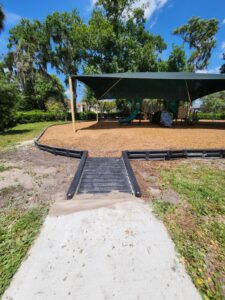 A pathway leading to a shaded area with a tent, surrounded by grass and trees, featuring a ramp for accessibility.