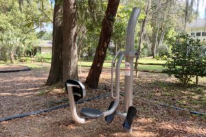 An outdoor exercise machine designed for fitness use, situated among trees and natural landscaping.