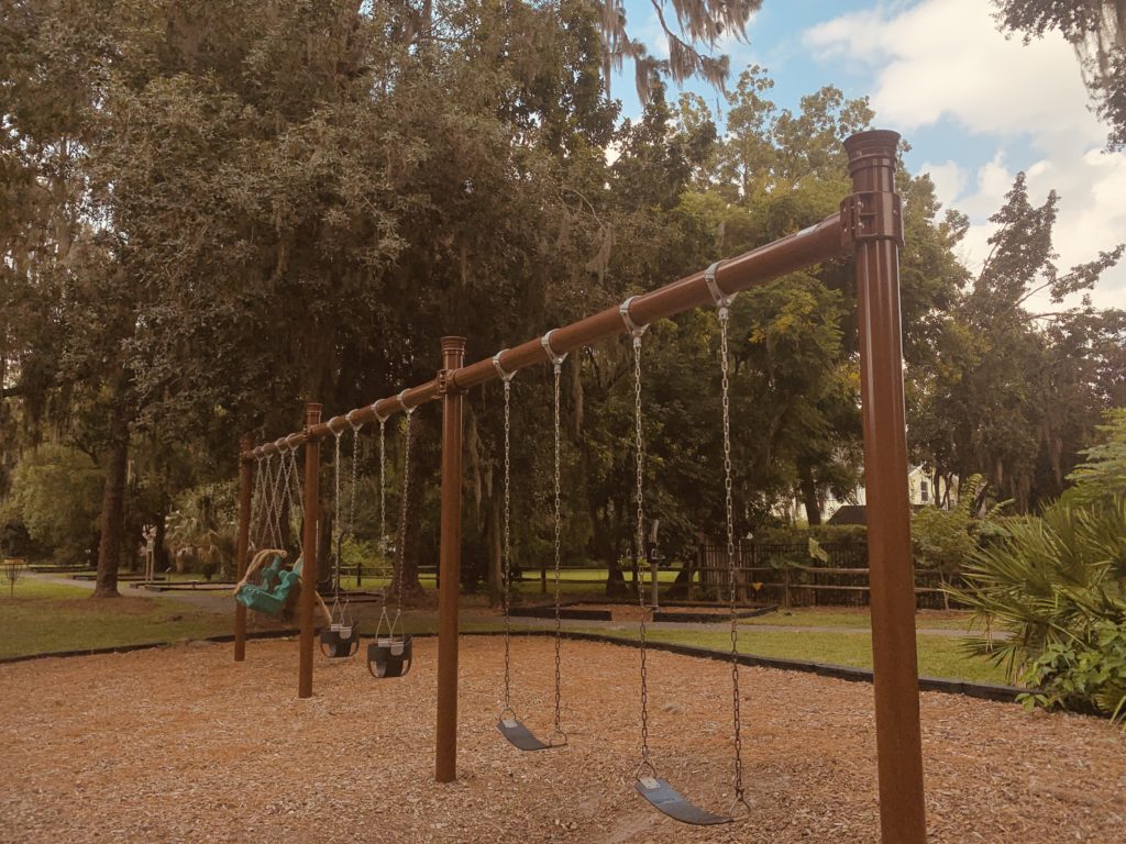 A playground featuring a row of swings set against a backdrop of trees and a clear sky.