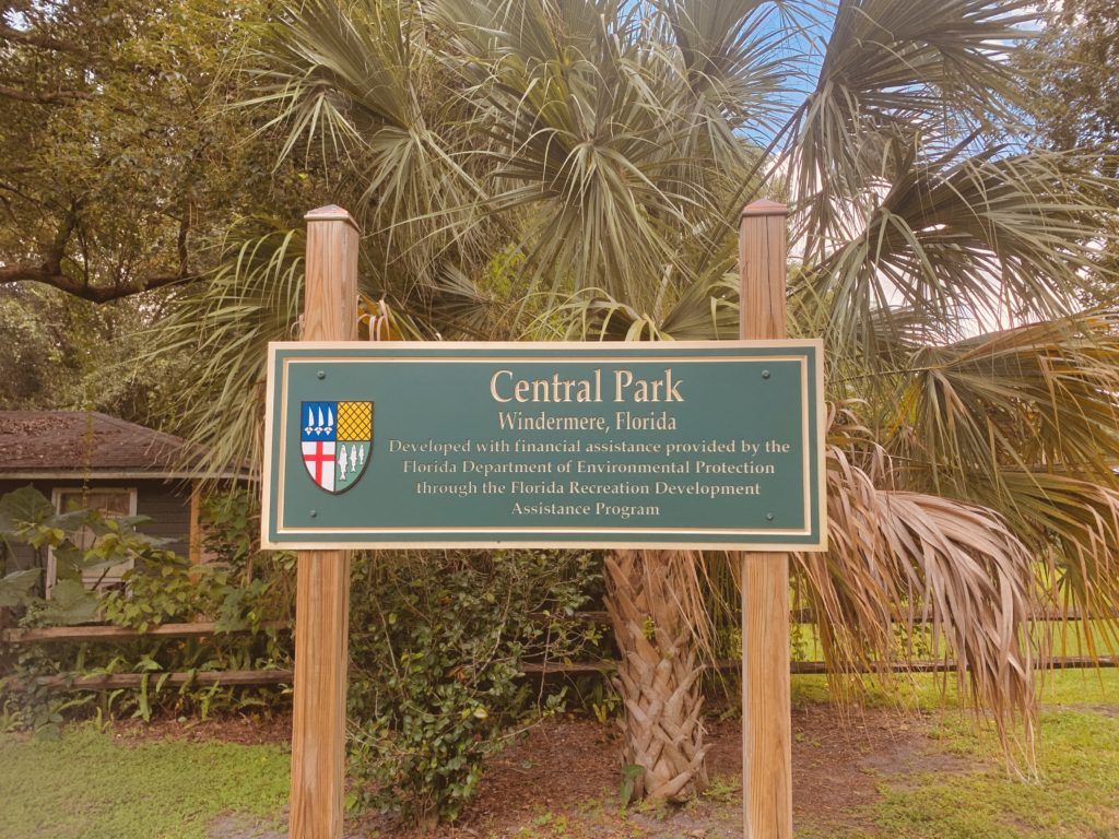 A green sign reading 'Central Park' in a park setting, surrounded by palm trees and grass, indicating the location in Wellington, Florida.