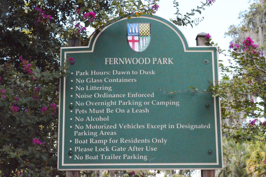 A green park sign listing rules and regulations for Fernwood Park, including hours of operation and restrictions on littering, noise, and vehicle access.