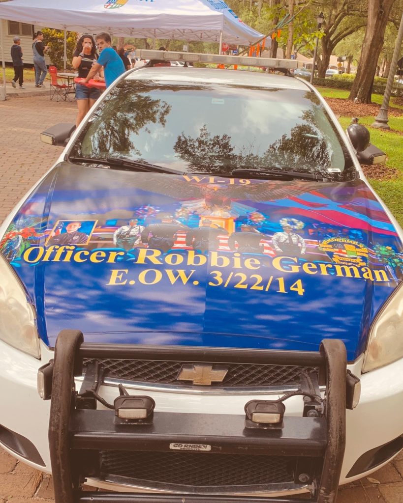 A police car featuring a colorful tribute to Officer Robbie German, with the text 'E.O.W. 3/22/14' displayed prominently on the hood.