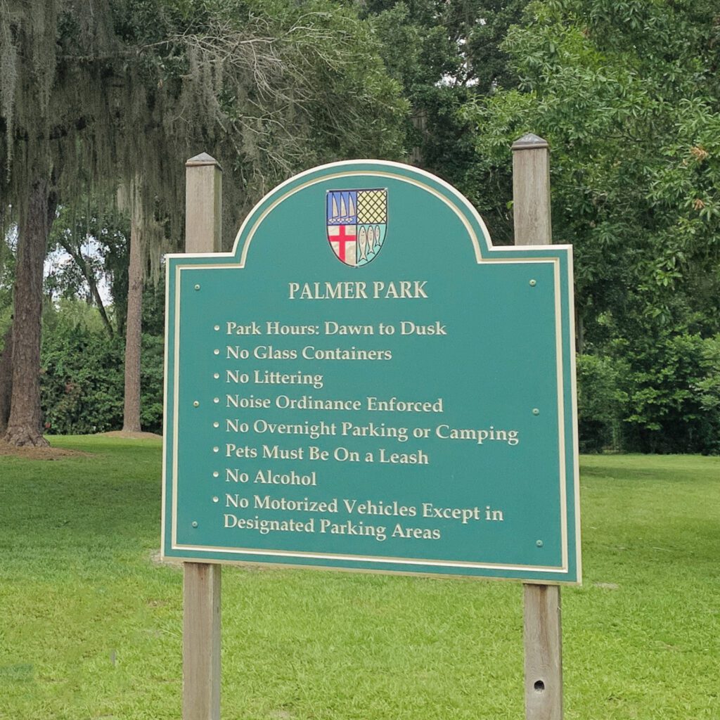 A green park sign listing rules for Palmer Park, including hours of operation, restrictions on glass containers, littering, overnight parking, pets, alcohol, and motorized vehicles.