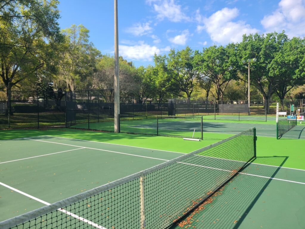 A view of several tennis courts surrounded by trees under a clear blue sky.