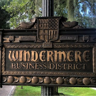 A decorative sign reading 'Windermere Business District' is mounted on a post, surrounded by lush greenery and trees.