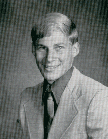 A black and white portrait of a young man with a light-colored suit and a tie, smiling at the camera.