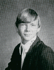 A black and white portrait of a young man with medium-length hair, wearing a suit and tie, looking directly at the camera with a slight smile.