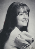 A young woman with long hair and a gentle smile poses for a portrait, wearing a light-colored top and holding a soft fabric close to her chest.