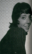 A black and white portrait of a young woman with short hair, smiling and looking over her shoulder.