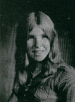 A black and white portrait of a young woman with long hair, smiling at the camera while wearing a collared shirt.