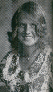 A black and white portrait of a smiling young woman with wavy hair, wearing a patterned dress with a lace collar.