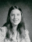 A black and white portrait of a young woman with long hair, smiling at the camera, wearing a floral-patterned blouse.