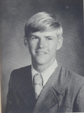 A black and white portrait of a young man with short, light-colored hair, wearing a suit and tie, smiling at the camera.