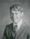 A black and white portrait of a young man with a slight smile, wearing a suit and tie, with short hair styled to the side.