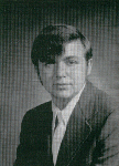 A black and white portrait of a man in a suit, with a side-parted hairstyle, looking directly at the camera.