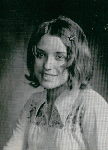 A black and white portrait of a young woman with shoulder-length hair, wearing a light-colored blouse with decorative embroidery, smiling softly at the camera.