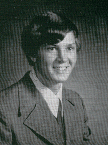 A black and white portrait of a young man with a smile, wearing a suit and tie, set against a plain background.
