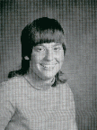 A black and white portrait of a young person with a distinctive hairstyle, smiling at the camera, wearing a long-sleeved shirt.
