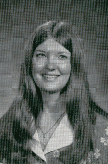 A black and white portrait of a young woman with long hair, smiling and wearing a collared shirt with floral patterns.