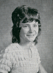 A black and white portrait of a young girl with a distinctive hairstyle, smiling at the camera, wearing a textured top.