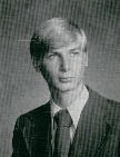 A black and white portrait of a young man with light-colored hair, wearing a suit and tie, looking directly at the camera.