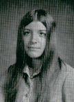 A black and white portrait of a young woman with long hair, wearing a collared shirt, looking directly at the camera.