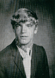 A black-and-white portrait of a young man with a distinctive hairstyle, wearing a suit and looking slightly to the side.