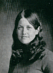 A black and white portrait of a young woman with long, wavy hair, wearing a turtleneck sweater, looking directly at the camera.