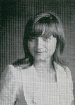 A black and white portrait of a young woman with long hair and bangs, wearing a light-colored blazer, set against a textured background.
