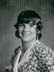 A black and white portrait of a smiling young woman with shoulder-length hair, wearing a floral-patterned blouse.