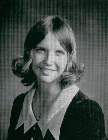 A black and white portrait of a young woman with shoulder-length hair styled in soft curls, wearing a dark dress with a white collar, smiling gently at the camera.