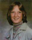 A young woman with shoulder-length hair, wearing a striped turtleneck and a light-colored jacket, smiles at the camera in a school portrait.
