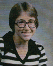 A young woman with short hair and large glasses smiles at the camera, wearing a black and white striped sweater.
