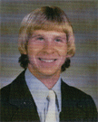 A young man with a distinctive hairstyle and a suit, smiling at the camera against a neutral background.