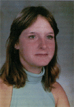A young woman with shoulder-length brown hair, wearing a light blue sleeveless top, poses for a school portrait against a gray background.