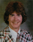 A young man with curly hair wearing a colorful plaid suit and tie, smiling at the camera.