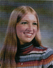 A smiling young woman with long, straight hair wearing a colorful striped sweater, posed against a blurred background.