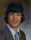 A young man with dark, wavy hair wearing a suit and tie, smiling at the camera in a formal portrait.