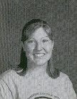 A black and white portrait of a smiling woman with shoulder-length hair, wearing a casual shirt, against a textured background.