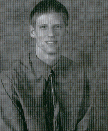 A black and white portrait of a young man wearing a collared shirt and tie, smiling at the camera.