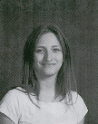 A young woman with long brown hair smiles at the camera, wearing a white shirt against a dark background.