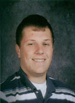 A young man with short hair and a friendly smile, wearing a striped shirt, poses for a school photo against a dark background.