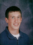 A young male student with short brown hair and a slight smile, wearing a blue collared shirt over a white t-shirt, posed against a dark background.